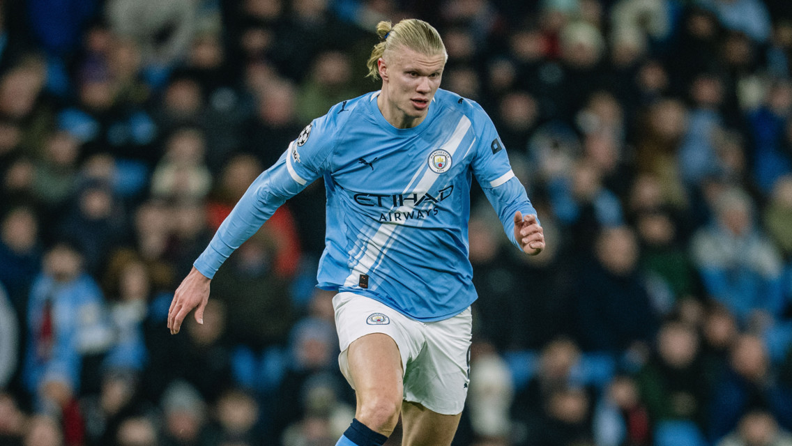 A football player wearing a Manchester City kit running on the field during a match with Etihad Airways sponsorship visible.