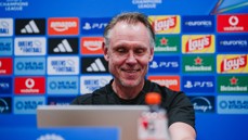 A man smiling at a computer during a press conference, with a backdrop featuring various sponsor logos such as Amazon, Adidas, Lay's, and Heineken.
