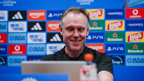 A man smiling at a computer during a press conference, with a backdrop featuring various sponsor logos such as Amazon, Adidas, Lay's, and Heineken.