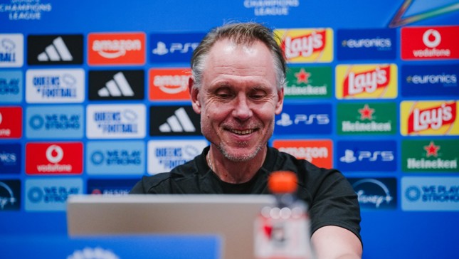 A man smiling at a computer during a press conference, with a backdrop featuring various sponsor logos such as Amazon, Adidas, Lay's, and Heineken.