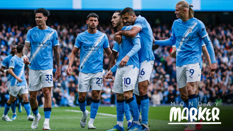 Manchester City players celebrate on the field, wearing light blue jerseys with Etihad Airways sponsorship. The scene suggests a goal celebration during a match at Etihad Stadium, with a crowd in the background and text saying Monday Marker.