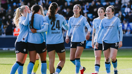 Manchester City women's team wearing light blue jerseys celebrating together on the field during a match.