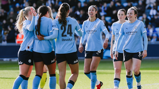 Manchester City women's team wearing light blue jerseys celebrating together on the field during a match.