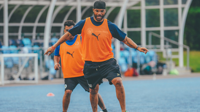 Two Manchester City players in training, wearing Puma apparel and orange bibs on a field.
