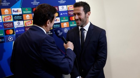 Two men in suits during an interview with a UEFA Champions League backdrop featuring various sponsor logos.