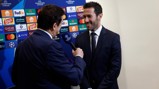 Two men in suits during an interview with a UEFA Champions League backdrop featuring various sponsor logos.