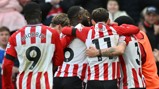 A group of football players in red and white striped jerseys celebrating, wearing jerseys numbered 9 and 11 with visible names 'BROBBEY' and 'RIGG'.