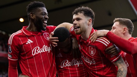 Four Nottingham Forest players in red striped jerseys celebrate a goal during a Premier League match.