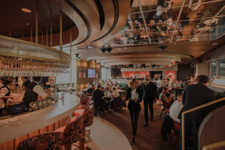 A lively restaurant interior with people dining and waitstaff serving, featuring a central bar area and mirrored ceiling.