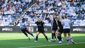 Women's soccer match action between Manchester City and Tottenham Hotspur teams with a player heading the ball. The crowd is watching from the stands.