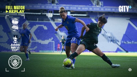 Two football players competing for the ball in a match at Birmingham City stadium. The event is part of the Adobe WFA Cup with Manchester City's involvement.