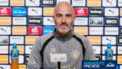 A bald man wearing a Manchester City jacket sits at a press conference table with sponsor logos like Etihad and Puma in the background.