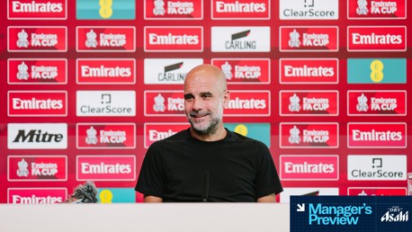 A person at a press conference with a red Emirates FA Cup background featuring logos like Mitre, ClearScore, Carling, and EE. There's a 'Manager's Preview' section sponsored by Asahi.