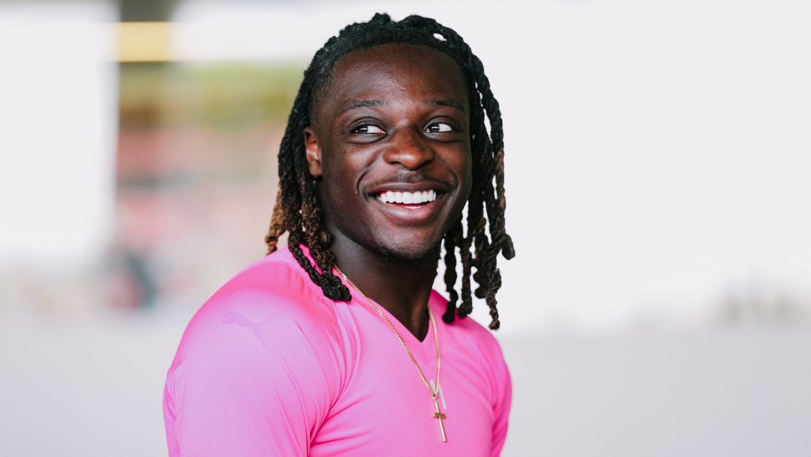 A person with long hair wearing a bright pink sports shirt and a gold cross necklace.