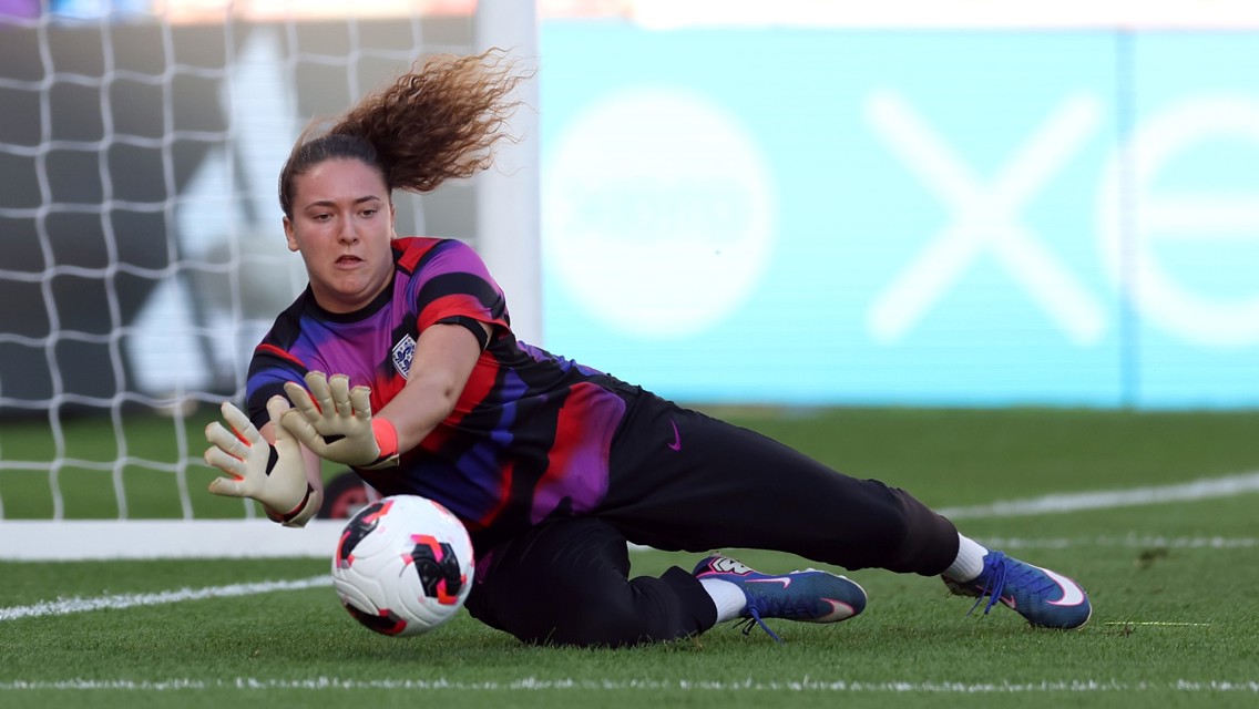 A goalkeeper diving to save a soccer ball during a practice session in front of a goal net on the field.