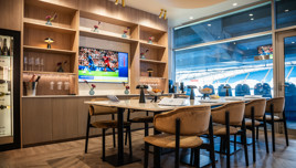 A luxury lounge with dining tables, a large screen displaying a sports channel, and a view of the stadium seats at Etihad Stadium.