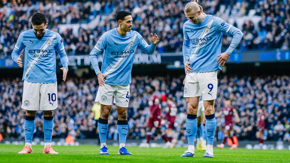 Three Manchester City players in home kit standing on the field during a match.