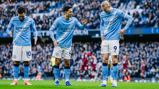 Three Manchester City players in home kit standing on the field during a match.