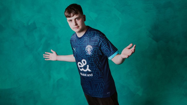 An individual wearing a Manchester City eSports jersey with outstretched arms against a teal background.