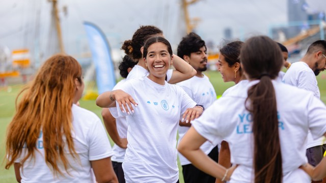 A group of young people in white shirts with blue logos interacting and smiling outdoors on a cloudy day.