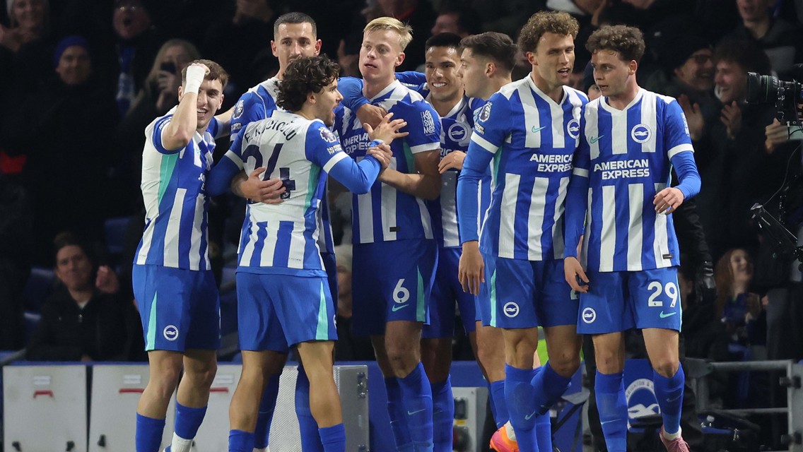 Players of Brighton & Hove Albion celebrating on the field wearing blue and white striped jerseys with 'American Express' branding.
