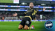 A football player wearing a black and yellow kit slides on his knees celebrating a goal, with a stadium crowd in the background. There is a digital scoreboard displaying 58:43.