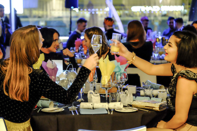 People toasting at a formal dinner event with blurred faces, set at a table with glasses, plates, and decorative napkins.