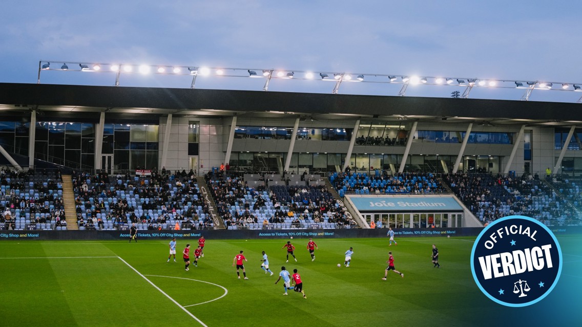 Football match at Joie Stadium with players from two teams on the field and audience in the stands.