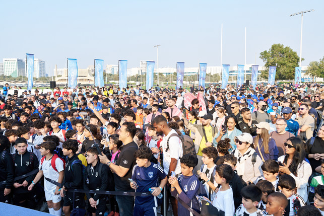 A large crowd gathered outdoors during the day, with banners showcasing the Manchester City logo in the background.