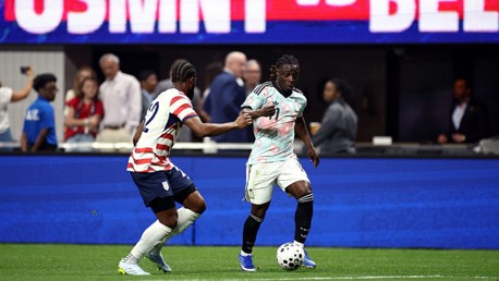 Two soccer players in action during a match, with one in a striped jersey and the other in a colorful jersey, both vying for the ball on the field.