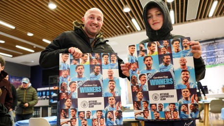Two individuals holding posters titled 'Carabao Cup Winners 2026' with blurred faces in a room.