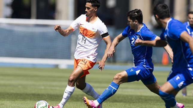 Players in orange and blue kits playing a soccer match on a grass field.