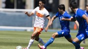 Players in orange and blue kits playing a soccer match on a grass field.