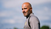 A bald man with a beard wearing a gray top with a Manchester City logo.