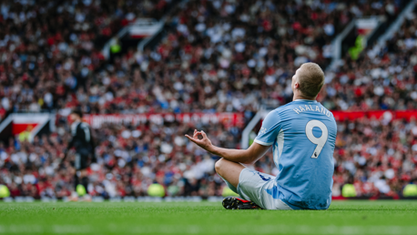 A player in a light blue Manchester City jersey with the name 'Haaland' and number '9' sits on the field in a meditation pose during a match.
