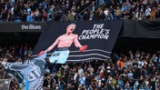 Fans at a stadium displaying a large banner with a boxer labeled 'HITMAN' and text 'THE PEOPLE'S CHAMPION'. The crowd is dressed in blue supporting the 'Blues'.