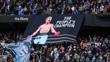 Fans at a stadium displaying a large banner with a boxer labeled 'HITMAN' and text 'THE PEOPLE'S CHAMPION'. The crowd is dressed in blue supporting the 'Blues'.