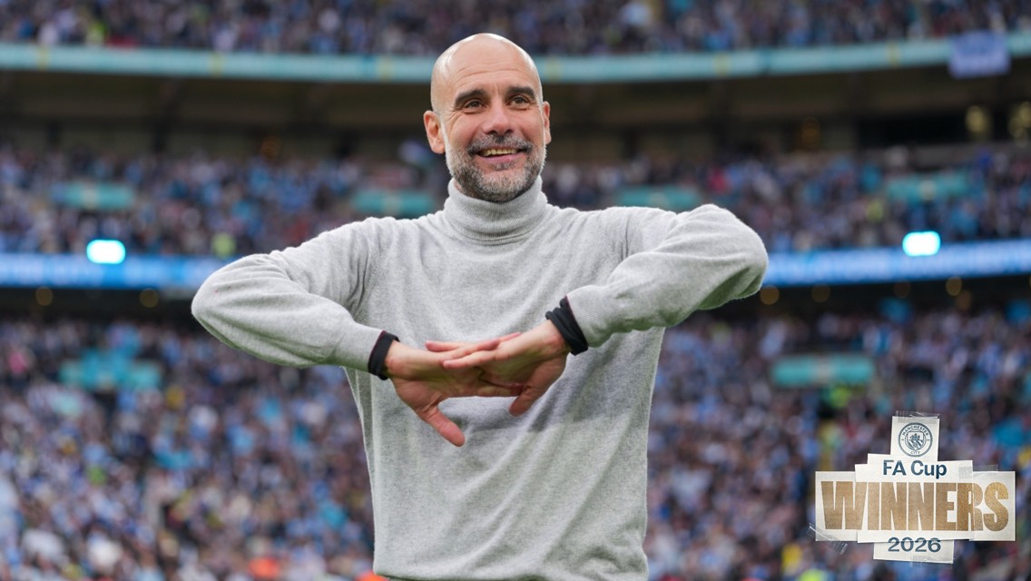 A person in a gray turtleneck sweater performing a gesture resembling crossed arms in front of a crowd. Overlay text reads 'FA Cup Winners 2026' with Manchester City crest.