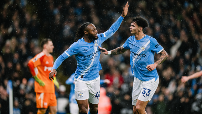 Two Manchester City players in blue kits celebrate a goal during a football match, with one player raising his arm for a high-five.