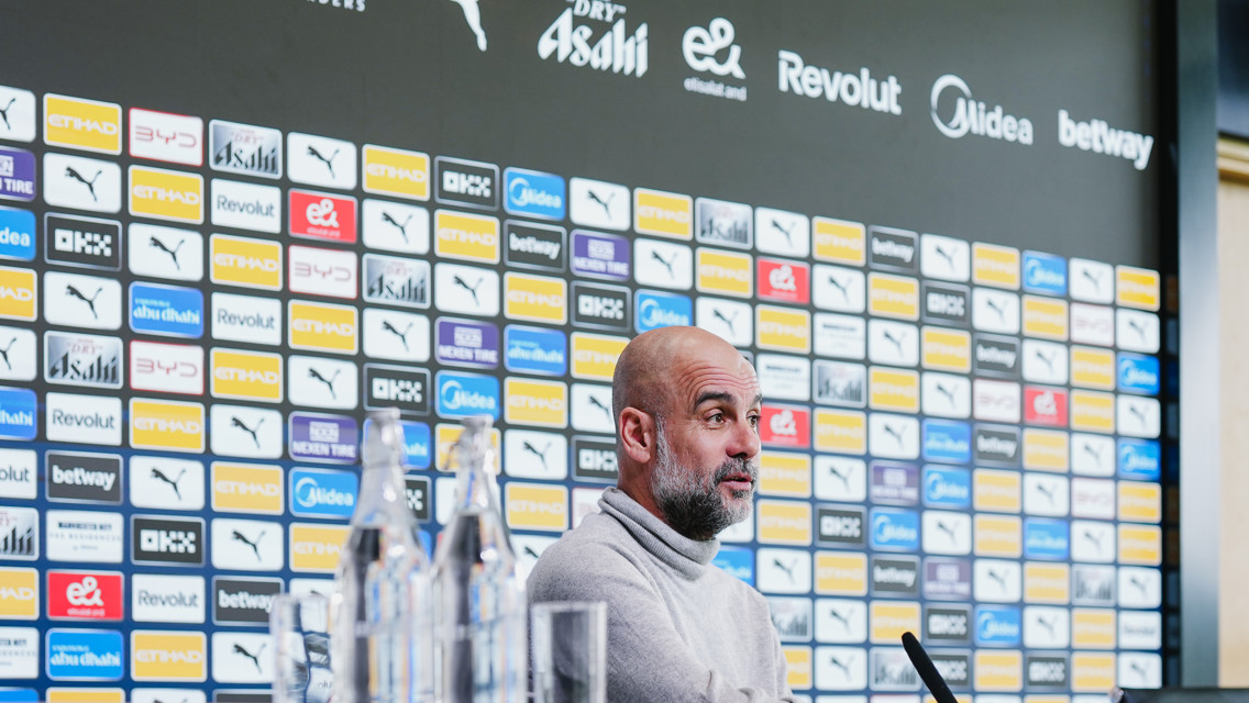 A person at a press conference seated in front of a backdrop with multiple sponsor logos, including Etihad and Puma, at Manchester City.