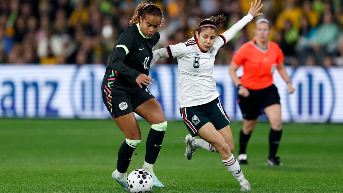 Two soccer players competing for the ball during a match, with a referee in the background.