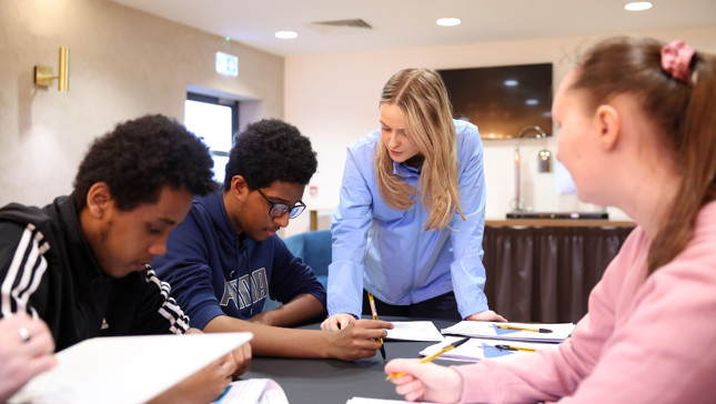 A teacher assists a group of students working on assignments in a classroom setting.