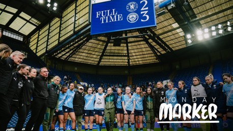 A soccer team, wearing light blue jerseys, celebrates on the field. The scoreboard shows the final score: Chelsea 2, Manchester City 3. The venue is a stadium with a prominent roof structure.