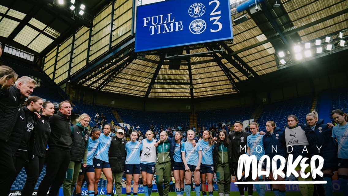A soccer team, wearing light blue jerseys, celebrates on the field. The scoreboard shows the final score: Chelsea 2, Manchester City 3. The venue is a stadium with a prominent roof structure.