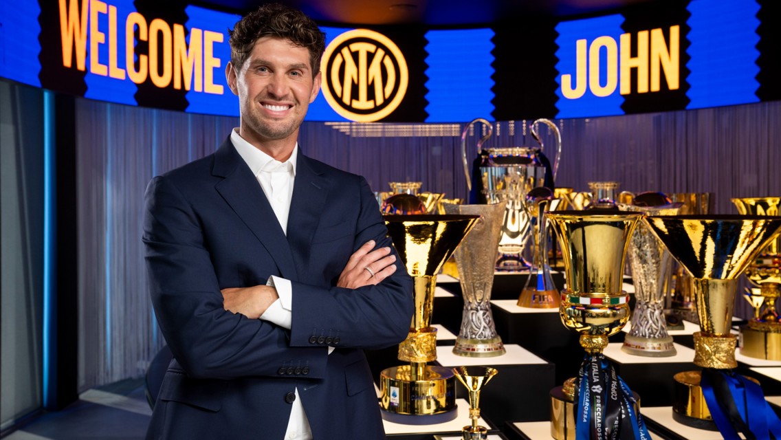 Man smiling in front of a trophy display. Background says 'Welcome John' with Inter logo.