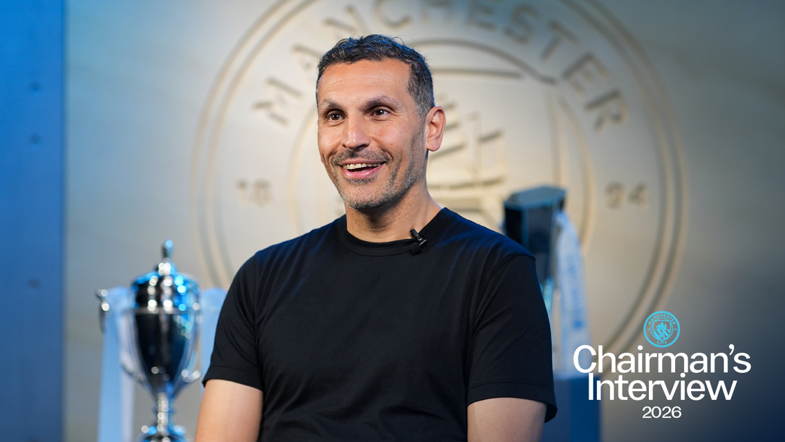 A person in a black shirt with a blurred face sits for an interview in front of a Manchester City logo and trophy display. The text 'Chairman's Interview 2026' is shown.