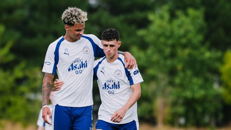 Two football players in Manchester City training gear walking together on a field.