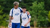Two football players in Manchester City training gear walking together on a field.