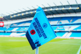 A corner flag at the Etihad Stadium features 'Manchester City Remembers', a poppy, and soldiers' silhouettes.