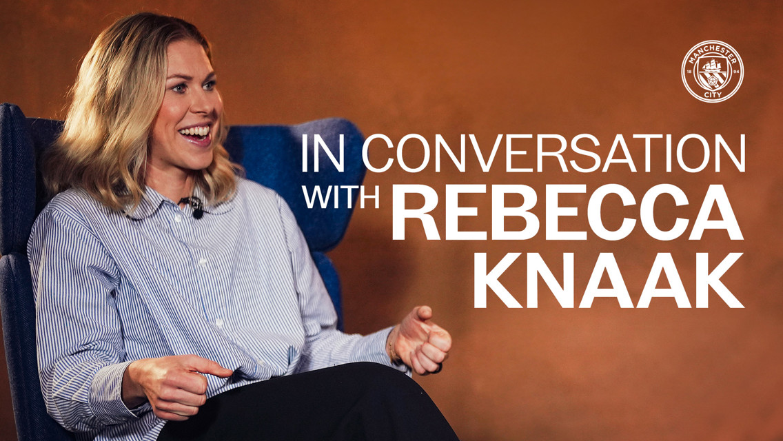 An interview setup with Rebecca Knaak's name shown, featuring the Manchester City logo in the background.